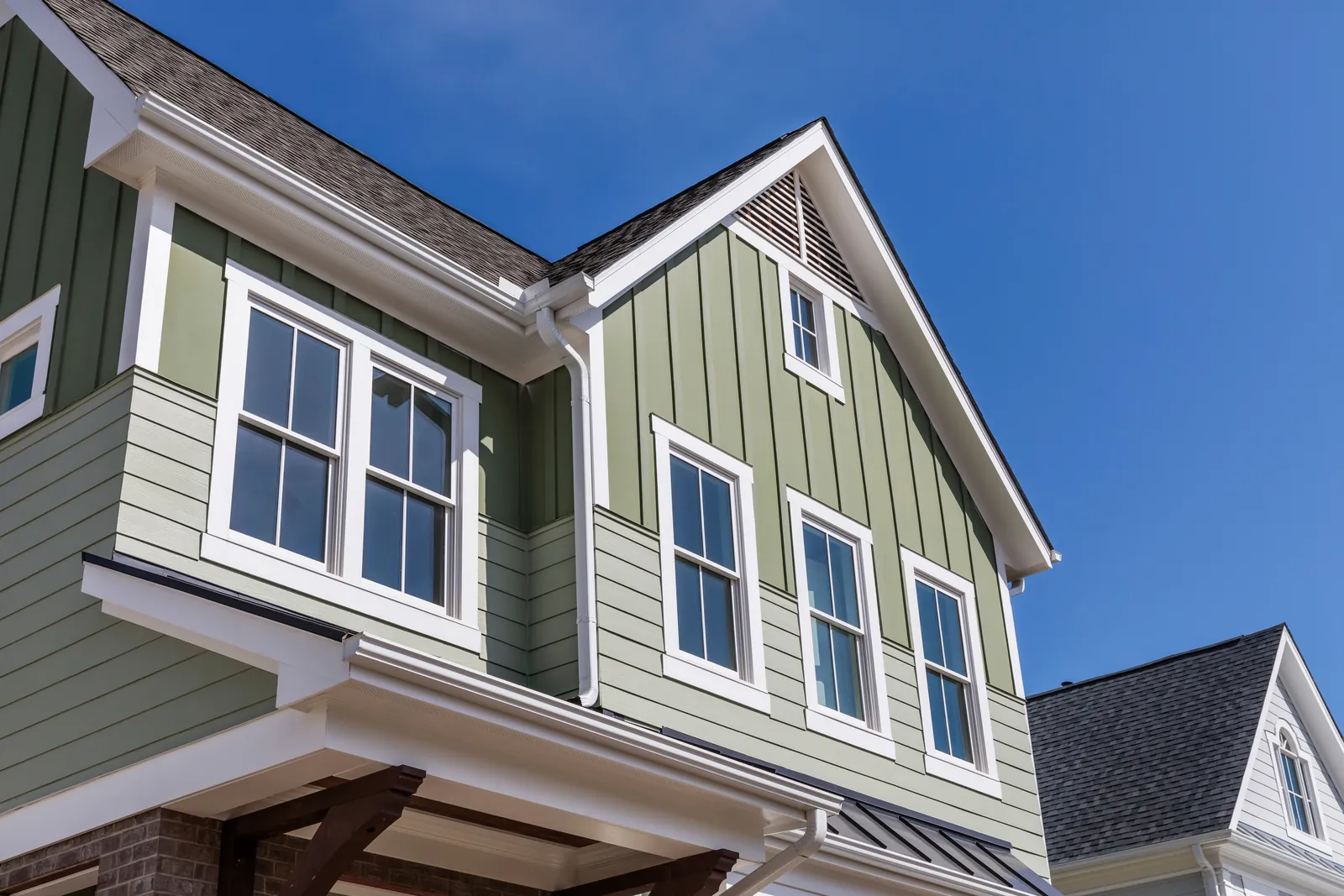 White gutters and a downspout along the roofline of a green-sided home