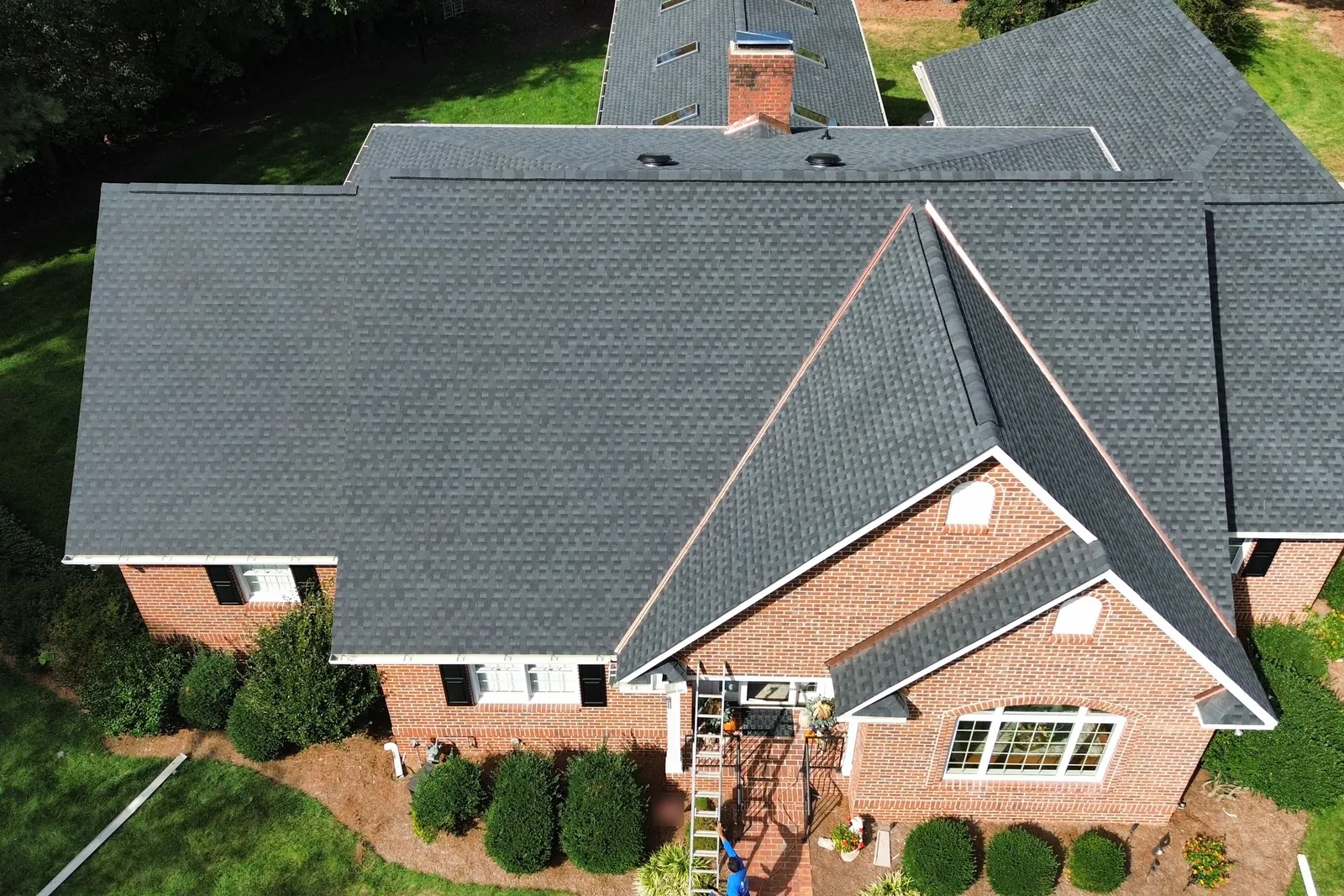 Aerial view of a finished gray asphalt shingle roof on a brick house
